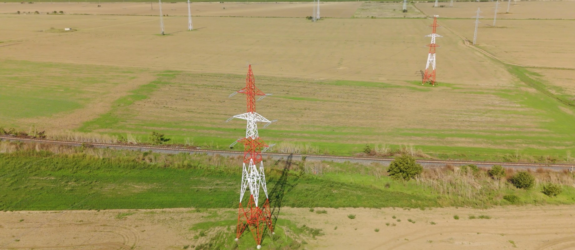 Stalp de inalta tensiune vopsit in rosu si alb, amplasat intr-o zona agricola deschisa, parte din reteaua de transport a energiei electrice gestionata de Retele Electrice